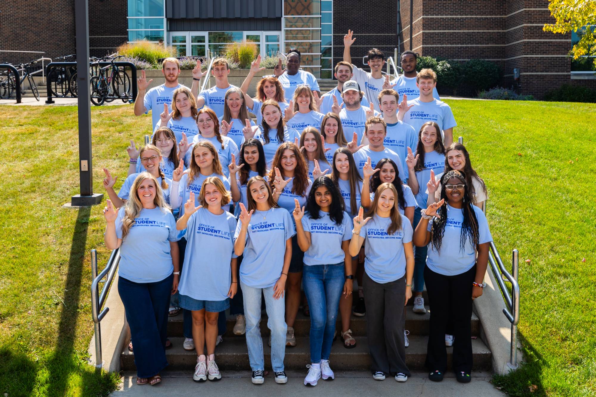 A group of staff wearing light blue Student Life t-shirts and raising the "anchor up" hand signal